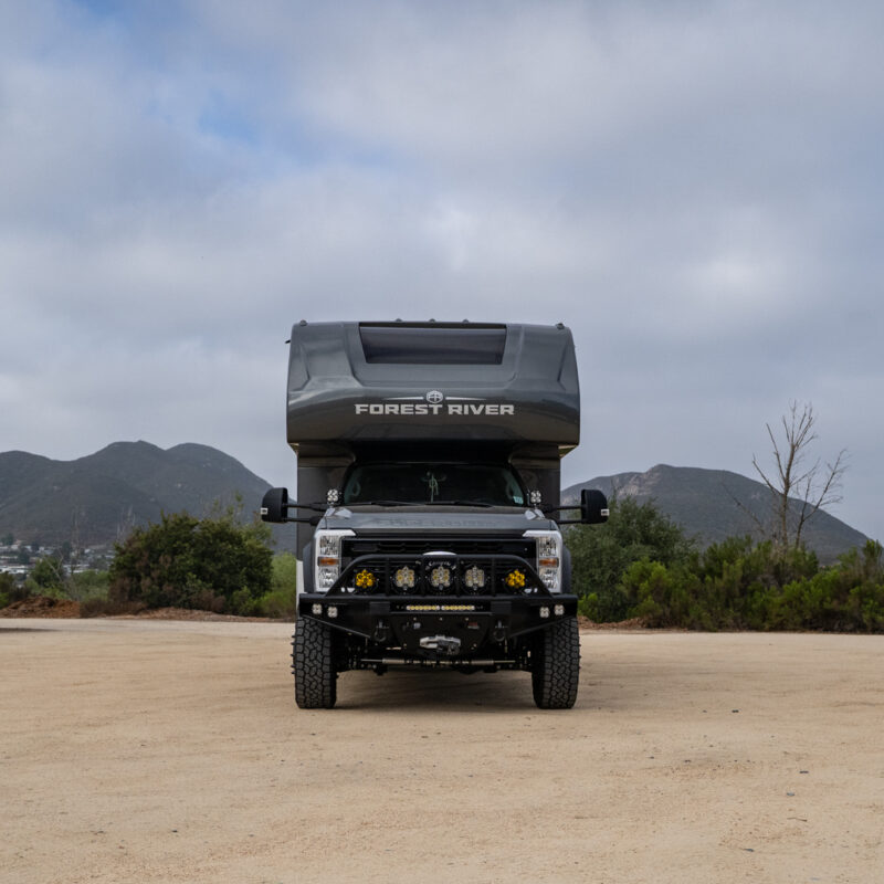 WeldTec Designs Sentinel front bumper installed on a Ford F-550/F-600 Forest River Super C RV with off-road tires, auxiliary LED lighting, and integrated winch.