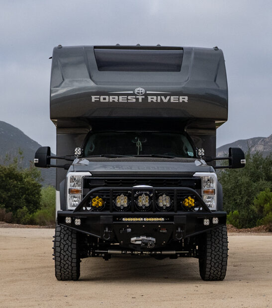 WeldTec Designs Sentinel front bumper installed on a Ford F-550/F-600 Forest River Super C RV with off-road tires, auxiliary LED lighting, and integrated winch.